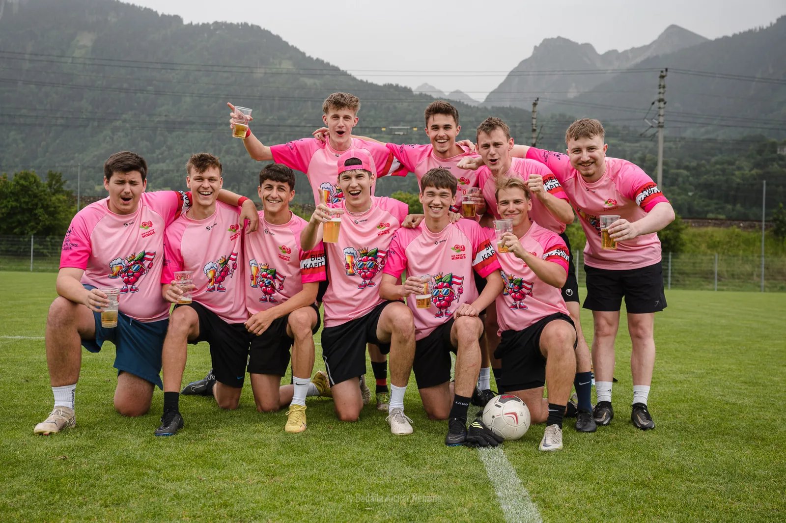 Die Harten Himbis in pinken Trikots als Mannschaft auf dem Fußballplatz vor den Bergen