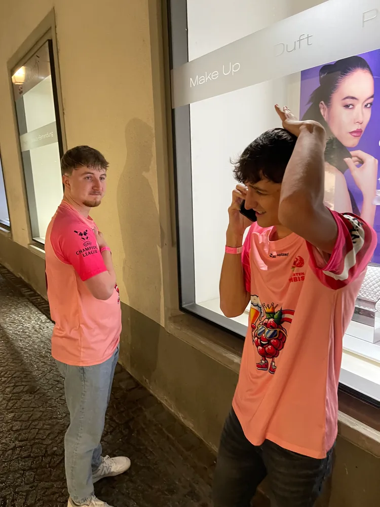 Zwei Himbis in pinken Trikots stehen abends gemeinsam vor einem Schaufenster